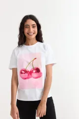 Remera de algodón color blanco, de corte clásico y manga corta, con estampa frontal de dos cerezas con textura de bola de boliche en tonos rosados.