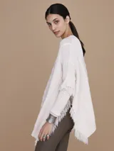 Mantela sweater color crudo, con cuello redondo y mangas largas con flecos. Tejido de punto con diseño de trenzas y bolsillos frontales.