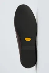 Mocasín de vestir en piel color marrón oscuro, con detalle de antifaz en el empeine, horma redonda y suela de goma Vibram.