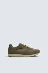 Zapatilla deportiva de estilo casual, confeccionada en una combinación de piezas de cuero con acabado de gamuza y paneles textiles. Presenta una horma redonda, cierre mediante cordones y una suela dentada en tono contrastante.