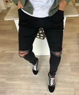 Pantalón chupín de jean color negro, de corte ajustado y diseño con roturas en las rodillas.