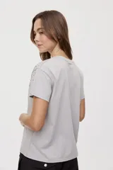 Remera de manga corta y cuello redondo color gris con efecto lavado, calce relajado y detalles de strass aplicados en la parte superior.