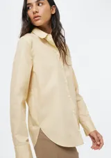 Camisa de corte clásico con cuello camisero, manga larga con puños vueltos y cierre frontal de botones. Presenta un diseño de rayas verticales finas en tono beige.