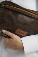 Riñonera de cuero marrón con textura envejecida, cierre metálico superior y parche frontal con el logo de la marca Nubia.