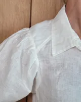 Camisa de lino color blanco con cuello camisero clásico, cierre frontal de botones y mangas largas abullonadas con puños anchos.