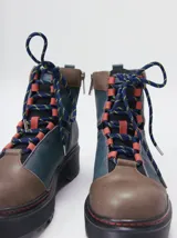 Bota de estilo trekking con diseño multicolor en tonos marrón, azul y detalles en rojo. Presenta plataforma de goma dentada, cordones tipo cuerda de escalada y cuello acolchado.