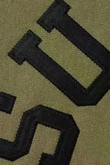 Hoodie de algodón color verde oliva con capucha y bolsillo tipo canguro. Presenta el logo de Supreme bordado en el pecho con tipografía arqueada y el logo de Champion bordado en la manga izquierda.