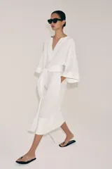 Vestido tipo túnica de corte evasé, color blanco, con escote en pico, mangas por debajo del codo y cinturón ajustable del mismo tejido.