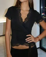 Remera negra de estilo cruzado con escote en V profundo, decorada con detalles de encaje en el borde del escote, mangas cortas y ruedo. Cuenta con un lazo lateral para ajuste.