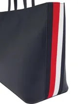 Cartera shopper azul marino de Tommy Hilfiger, confeccionada en poliuretano con doble asa superior y cierre de cremallera. Presenta el logotipo metálico de la marca en la parte delantera.