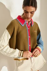 Cardigan de punto con diseño colorblock, cuerpo marrón, manga derecha blanca en punto trenzado y manga izquierda celeste también en punto trenzado. Cuenta con cuello polo en color fucsia con ribete celeste, cierre frontal con botones y detalles de rayas en los puños y el ruedo.