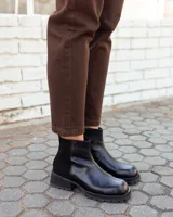 Botinetas de cuero negro con paneles laterales de gamuza al tono. Presentan una suela track robusta con taco cuadrado y cierre lateral para facilitar el calce.