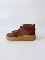 Zapatillas acordonadas de cuero marrón con detalles en rojo y suela de goma color caramelo.