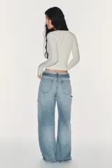 Jeans de mezclilla de tiro medio, corte wide leg y diseño relaxed. Presenta detalles rotos y desgastados en las piernas, y una cinturilla doblada superpuesta con trabillas y cierre frontal con cremallera y botón metálico.