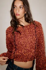 Jersey de punto grueso con textura trenzada en color naranja y bordó. Presenta cuello redondo, mangas largas abullonadas y detalle de cordones trenzados a contraste en el frente con terminación en lazada en el ruedo.