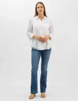 Camisa de tencel color blanco, con cuello camisero, cierre frontal de botones y dos bolsillos en el pecho. Presenta mangas largas con presilla para regular el largo y ruedo con detalle de flecos.
