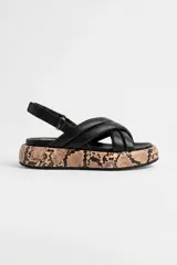 Sandalia de cuero ovino color negro, con tiras acolchadas cruzadas en el empeine y tira trasera con hebilla ajustable. Cuenta con una plataforma plana revestida con estampado de piel de serpiente.