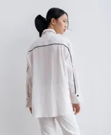 Camisa negra de manga larga, con cuello camisero y botones frontales. Presenta aberturas laterales en el ruedo.