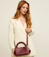 Cartera pequeña color bordó, con asa de mano trenzada y estructura rígida de líneas redondeadas.