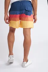 Short de baño con cintura elástica y cordón ajustable, confeccionado en tela ligera de secado rápido. Presenta un estampado botánico integral en tonos amarillos, blancos y azules, con dos bolsillos delanteros y uno posterior.