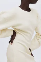 Vestido corto de punto acanalado con cuello redondo, hombros caídos y mangas largas de gran volumen con diseño curvado. Presenta un ajuste entallado en el cuerpo y falda con ligero vuelo.