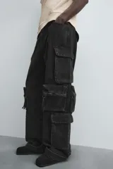 Pantalón cargo de denim lavado negro, corte relajado y tiro medio. Presenta múltiples bolsillos cargo con solapa y detalle de cierre en las perneras, además de bolsillos de vivo traseros. El bajo es ajustable con trabilla.