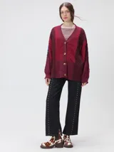 Cardigan oversize de tejido de punto grueso con diseño de bloques de color en tonos tierra. Presenta cuello en V, cierre frontal con botones, mangas largas con terminación abullonada y parches decorativos en el pecho y hombro.