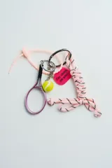 Llavero con dije de raqueta de tenis violeta, pelota de tenis amarilla, dije rosa con la frase "I'm stuck on you!" y cordón trenzado rosa con detalles en negro.