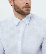 Camisa de corte comfort, manga larga con cuello camisero y cierre frontal de botones. Presenta un estampado de cuadros tipo grid en tonos claros sobre fondo blanco.