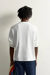 Camiseta de manga larga color azul con cuello redondo, corte relajado y pequeño parche gráfico bordado en el pecho.