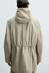 Parka de corte regular confeccionada en tejido de algodón ligero con efecto lavado. Presenta cuello subido con capucha ajustable mediante cordones, cierre frontal con botones y manga larga con puños ajustables con trabilla. Incluye bolsillos de plastrón con solapa en la cadera y cintura ajustable con cordón interior.