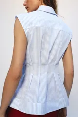 Camisa de algodón sin mangas con cuello solapa, diseño a rayas celestes y blancas, pliegues en la cintura y bajo evasé. Cierre frontal con botones ocultos.
