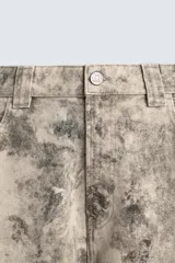 Pantalón de corte relajado confeccionado en algodón, con diseño de efecto lavado y estampado abstracto en tonos grises y beige. Presenta cinco bolsillos y cierre frontal con cremallera y botón.