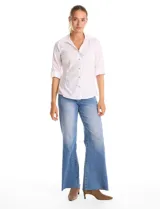 Camisa blanca de algodón con cuello solapa, escote en V y cierre frontal con botones decorativos de strass. Presenta pinzas de entalle para un ajuste definido, mangas tres cuartos con terminación rebatible y ruedo redondeado.