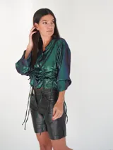 Camisa negra de satén con brillo satinado, escote en V, mangas largas y botones de nácar. Cuenta con cordones laterales ajustables para fruncir la prenda.