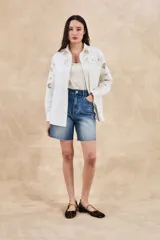 Sobrecamisa blanca de algodón con bordados florales calados en mangas, cuello y pechera. Corte oversize, manga larga y dos bolsillos frontales.