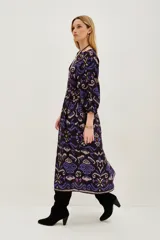 Vestido midi de viscosa con estampado estilo ikat en tonos oscuros, violetas y azules. Presenta mangas largas, cuello redondo y un diseño holgado que se ajusta a la cintura mediante un cinturón.