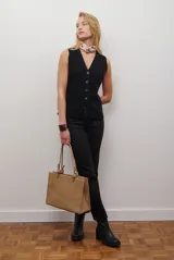 Chaleco tejido de punto en color beige, con escote en V, cierre frontal con botones oscuros y bolsillos frontales decorativos.