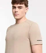 Remera deportiva de hombre con tecnología dry fit, cuello redondo y manga corta. Presenta un diseño liso en color beige con una pequeña etiqueta decorativa en el dobladillo.