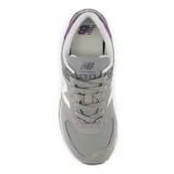 Championes urbanos New Balance modelo 574, color gris con detalles en blanco y panel metalizado violeta en el talón. Confeccionados en gamuza y malla, cuentan con entresuela ENCAP para mayor amortiguación y suela de goma.