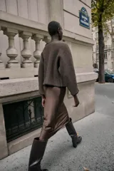 Jersey de punto color marrón con cuello barco y manga larga. Presenta pespuntes decorativos en color negro a contraste en el cuello, puños y bajo.