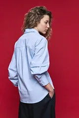 Camisa blanca de manga larga con volumen y estructura, cierre frontal con botones y lazo ajustable en la cintura que realza la silueta.