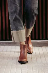 Botín de cuero negro, caña corta, con punta cuadrada y cierre lateral. Presenta un tacón de madera de altura media y detalles en charol con textura de cocodrilo en el talón.