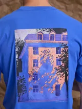 Remera de manga corta color azul con estampa artística en la espalda que representa una fachada de edificio con sombras.