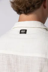 Camisa de hombre de manga corta color beige claro, confeccionada en lino. Tiene cuello clásico, cierre frontal con botones y corte recto.