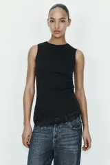 Camiseta ajustada (slim fit) color crema, con cuello redondo y mangas sisa. Presenta frunces laterales y un bajo asimétrico con detalle de encaje a tono.