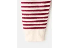 Chaleco de punto color marfil con cuello polo, escote en V y diseño de rayas horizontales burdeos en el pecho y las mangas. Cuenta con mangas largas y un diseño holgado, ideal para usar superpuesto o anudado.