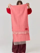 Bufanda de gran tamaño en color mostaza con diseño de tejido en espiga y flecos en los extremos. Incluye una etiqueta metálica decorativa en una de las esquinas.