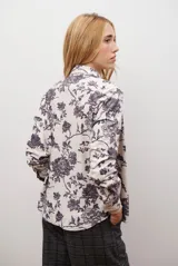 Camisa de manga larga con cuello clásico y cierre frontal de botones. Presenta un estampado floral en tonos marrones sobre una base color beige, confeccionada en un tejido con textura similar al gamuzado.