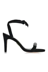 Sandalia negra de gamuza con taco aguja, tira delgada sobre los dedos con detalle de esfera brillante y tira fina que se ata al tobillo.